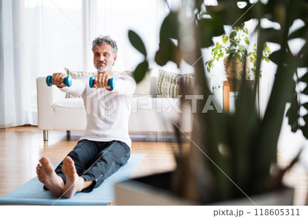 Handsome man exercising at home on gym mat. Routine home workout for a middle-aged man. Handsome man exercising at home on gym mat. Routine home workout for a middle-aged man. 118605311