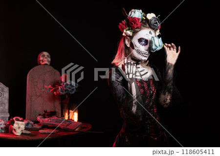 Mysterious woman covering eye with rose during Day of the Dead Halloween event honoring dead loved ones. Eerie lady being enigmatic during ancient Aztec custom of celebrating ancestors Mysterious woman covering eye with rose during Day of the Dead Halloween event honoring dead loved ones. Eerie lady being enigmatic during ancient Aztec custom of celebrating ancestors 118605411