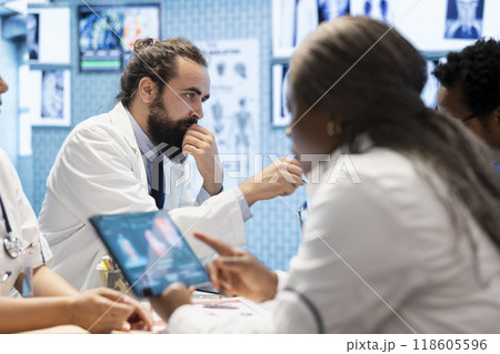 Medical professionals in a meeting examining organs on ct scan results. Skilled physicians and radiologists review x rays and hospital records to develop effective treatment plans. Collective work. Medical professionals in a meeting examining organs on ct scan results. Skilled physicians and radiologists review x rays and hospital records to develop effective treatment plans. Collective work. 118605596