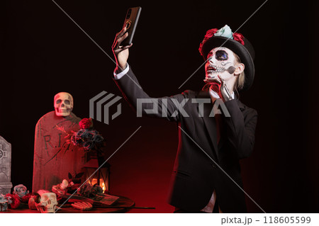 Woman taking selfie pictures with phone during Day of the Dead Mexican event honoring dead loved ones. Person posing for smartphone photos during ancient Aztec custom of celebrating ancestors Woman taking selfie pictures with phone during Day of the Dead Mexican event honoring dead loved ones. Person posing for smartphone photos during ancient Aztec custom of celebrating ancestors 118605599