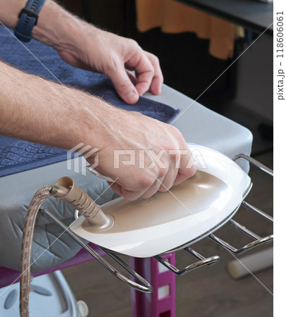 Man irons towel and clothes with steam iron on modern ironing table. Cleanliness and care of clothes at home. Household appliances.  118606061