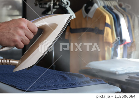 Man irons towel and clothes with steam iron on modern ironing table. Cleanliness and care of clothes at home. Household appliances.  118606064