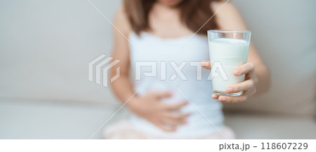 Lactose intolerance and Milk allergy concept. woman hold Milk glass and having abdominal cramps and pain when drink Cow Milk. Symptom stomach ache, Dairy intolerant, Nausea, Bloating, Gas and Diarrhea 118607229