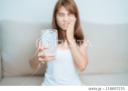 Teeth Sensitive to Cold concept. woman hold Ice Water glass and having toothache and pain after eat. Tooth Decay or Gum Disease, Grinding Teeth and Stress, Exposed Nerve Roots, Crack and Receding Gums Teeth Sensitive to Cold concept. woman hold Ice Water glass and having toothache and pain after eat. Tooth Decay or Gum Disease, Grinding Teeth and Stress, Exposed Nerve Roots, Crack and Receding Gums 118607235