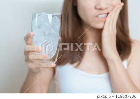Teeth Sensitive to Cold concept. woman hold Ice Water glass and having toothache and pain after eat. Tooth Decay or Gum Disease, Grinding Teeth and Stress, Exposed Nerve Roots, Crack and Receding Gums 118607236