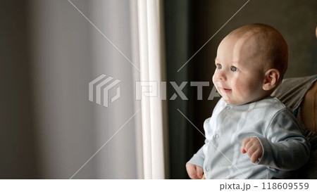 Young woman holding a small child in arms while standing by the window. Mom holds a small child by the window. 118609559