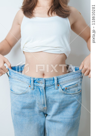 young slim female wearing big or oversize jeans, woman show healthy shape after weight loss. dieting, exercise, body fit and liposuction surgery concept young slim female wearing big or oversize jeans, woman show healthy shape after weight loss. dieting, exercise, body fit and liposuction surgery concept 118610281