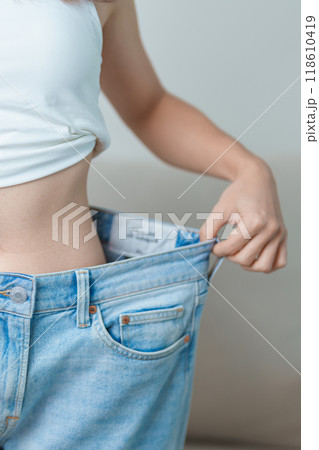 young slim female wearing big or oversize jeans, woman show healthy shape after weight loss. dieting, exercise, body fit and liposuction surgery concept young slim female wearing big or oversize jeans, woman show healthy shape after weight loss. dieting, exercise, body fit and liposuction surgery concept 118610419