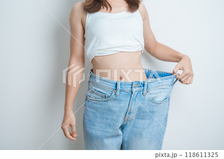 young slim female wearing big or oversize jeans, woman show healthy shape after weight loss. dieting, exercise, body fit and liposuction surgery concept young slim female wearing big or oversize jeans, woman show healthy shape after weight loss. dieting, exercise, body fit and liposuction surgery concept 118611325