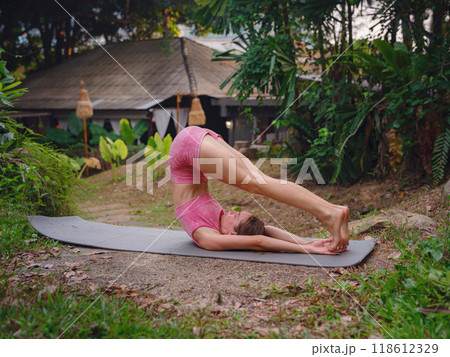 Beautiful woman practices yoga by pool in morning in Thailand. Young female in sportswear in hotel exotic garden. perfect flexible body recreating doing yoga poses feeling inner peace and vitality 118612329