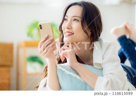 リビングのテーブルで寝転んでスマホを見る若い女性 リビングのテーブルで寝転んでスマホを見る若い女性 118613099