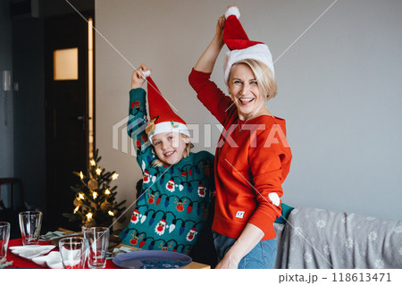 Mother and daughter setting the table for Christmas dinner, holiday meal preparation, festive family traditions, Christmas Eve, quality time, togetherness. 118613471