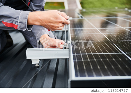 Man installer mounting photovoltaic solar panels on roof of house. Close up view of engineer installing solar module system with help of hex key. Concept of alternative, renewable energy. Man installer mounting photovoltaic solar panels on roof of house. Close up view of engineer installing solar module system with help of hex key. Concept of alternative, renewable energy. 118614737