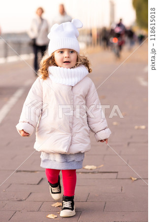 Little funny girl runs and smiles on yellow trees background in the autumn park. Preschool girl running and laughing on the park alley Little funny girl runs and smiles on yellow trees background in the autumn park. Preschool girl running and laughing on the park alley 118615018
