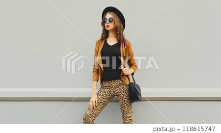 Beautiful stylish young woman posing with handbag in black hat, jacket, glasses on city street Beautiful stylish young woman posing with handbag in black hat, jacket, glasses on city street 118615747