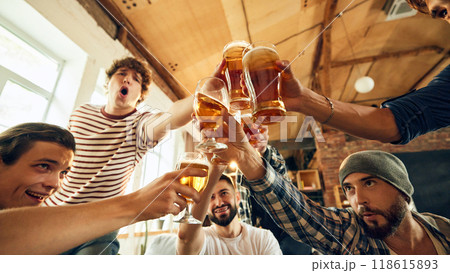 Celebration hits high as all guys raise their glasses for victory toast. Table full of snacks and drinks testament to fun they're having. 118615893