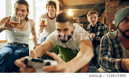 Game night chaos, one friend totally focused, gripping his controller, while others can't help but burst into laughter. 118615900