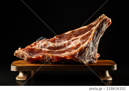 Large piece of dry cured ham on wooden stand on black background 118616102