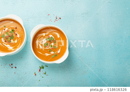 Two bowls of creamy pumpkin soup decorated with parsley and pepper on blue background top view copy space 118616326