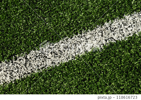 Artificial green grass with white stripe of soccer field. Outdoors. Summer. View from above. Artificial green grass with white stripe of soccer field. Outdoors. Summer. View from above. 118616723