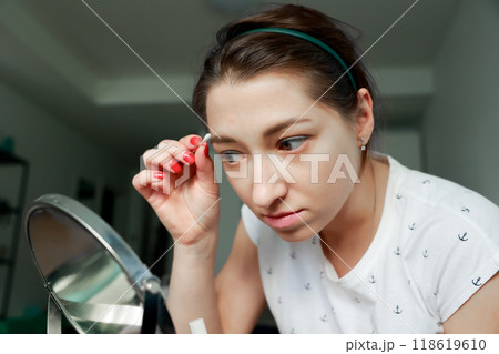 Young girl correcting her makeup in front of the mirror. Home makeup and self-care concept. 118619610