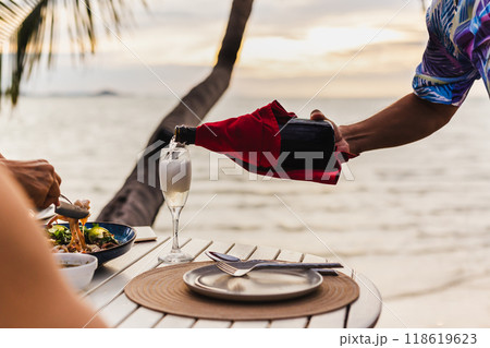 Waiter pouring champagne in a glass with food on table. Waiter pouring champagne in a glass with food on table. 118619623