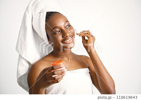 Black young woman in a white bathrobe isolated on white background. Girl has her hair wrapped in a towel. Black woman enjoy after body treatment. Black young woman in a white bathrobe isolated on white background. Girl has her hair wrapped in a towel. Black woman enjoy after body treatment. 118619643