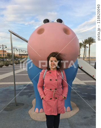 Young woman enjoying a delightful playful moment with a charming blue and pink hippo sculpture found in the playground 118620040