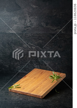 Empty cutting board with rosemary on a black stone background. 118620836