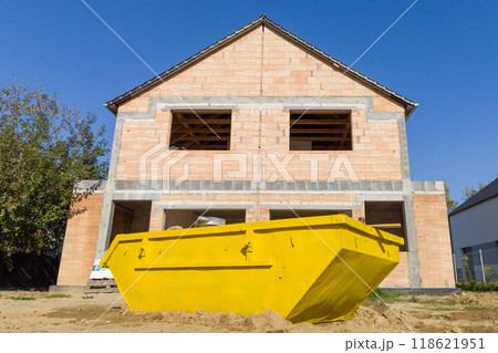 Unfinished brick house with yellow construction skip for waste disposal 118621951