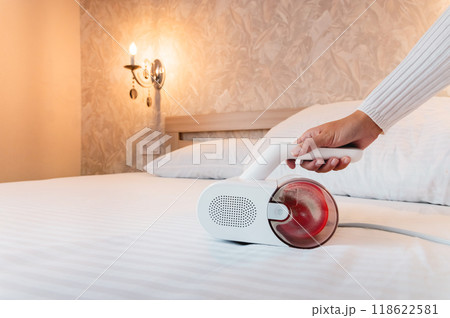 Vacuum cleaner for cleaning mattresses from mites with UV lamp and knocking out dust. A woman's hand is cleaning and disinfecting a mattress in the bedroom Vacuum cleaner for cleaning mattresses from mites with UV lamp and knocking out dust. A woman's hand is cleaning and disinfecting a mattress in the bedroom 118622581
