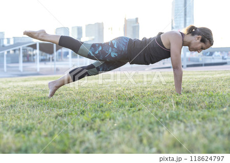 Woman performing plank exercise on grass in city park... Woman performing plank exercise on grass in city park... 118624797