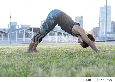 Woman doing downward dog yoga pose in a city park... Woman doing downward dog yoga pose in a city park... 118624799