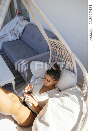 Experience relaxation while sitting in a Cozy Hanging Chair, enjoying your Smartphone 118625481