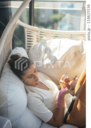 A Relaxing Woman Using Her Phone in a Cozy Indoor Setting That Enhances Comfort and Serenity 118625536