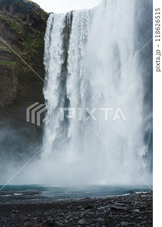 Experience the powerful Skogafoss waterfall in Iceland, with its 60-meter drop, green moss-covered cliffs, and serene basin. A must-see natural landmark. 118626515