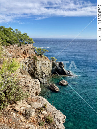 View of a rocky seashore with a horizon line and a blue sky with clouds in Phaselis, Kemer, Turkey View of a rocky seashore with a horizon line and a blue sky with clouds in Phaselis, Kemer, Turkey 118626767