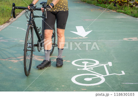 Cropped shot of female cyclist holding her road bike before riding on bicycle lane in the park. Cropped shot of female cyclist holding her road bike before riding on bicycle lane in the park. 118630103