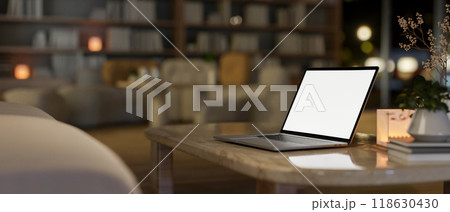 A laptop on a coffee table in a contemporary living room, illuminated by warm lighting. 118630430