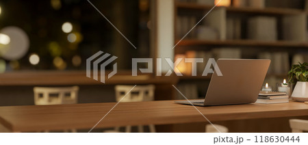 A laptop on a wooden table in a minimalist coffee shop at night, illuminated by the warm lights. A laptop on a wooden table in a minimalist coffee shop at night, illuminated by the warm lights. 118630444