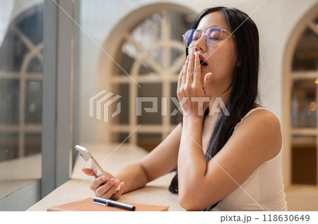 A beautiful Asian woman, feeling tired and sleepy, sits in a stunning coffee shop. A beautiful Asian woman, feeling tired and sleepy, sits in a stunning coffee shop. 118630649