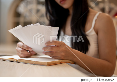A close-up of a thoughtful Asian woman reviewing receipts in her hand, managing her expenses. A close-up of a thoughtful Asian woman reviewing receipts in her hand, managing her expenses. 118630652