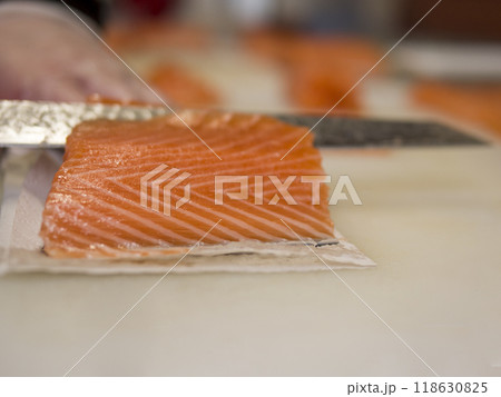 With expert hands, the chef slices fresh salmon into even pieces The sharp knife moves smoothly through the salmon, creating perfect portions that display the skill behind preparing salmon. With expert hands, the chef slices fresh salmon into even pieces The sharp knife moves smoothly through the salmon, creating perfect portions that display the skill behind preparing salmon. 118630825