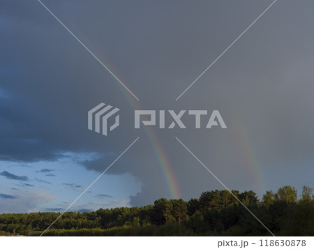 Amid dark clouds, a brilliant rainbow emerges its colors vivid against the stormy backdrop. As the rainbow stretches across the sky, the contrast with the clouds enhances the scene's dramatic beauty. 118630878