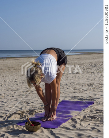 Yoga strengthens both body and mind as a young blonde woman stretches on beach mat by sea She focuses on each yoga movement, enhancing flexibility and warming up her muscles. vertical photo Yoga strengthens both body and mind as a young blonde woman stretches on beach mat by sea She focuses on each yoga movement, enhancing flexibility and warming up her muscles. vertical photo 118630981