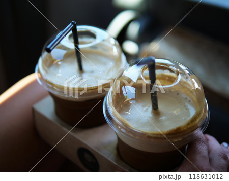 Two cold coffees with black straws in plastic cups stand in cup holders ready to refresh. These cold coffees are perfect for cooling down and savoring a delicious, iced beverage Refreshing effect 118631012