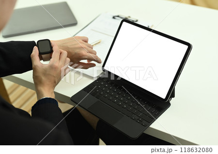 Cropped shot businessman checking time on smartwatch and using digital tablet at desk Cropped shot businessman checking time on smartwatch and using digital tablet at desk 118632080