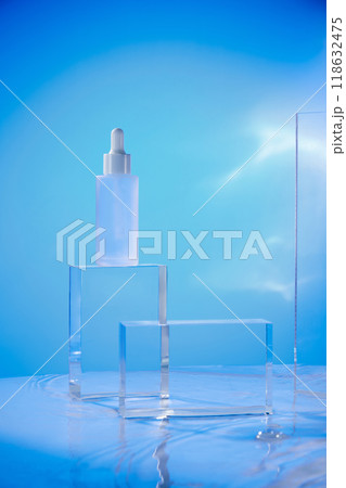 A transparent acrylic pedestal holds a dropper bottle filled with serum, which reflects light onto the water's surface. The soft blue background is ideal for beauty product advertising. A transparent acrylic pedestal holds a dropper bottle filled with serum, which reflects light onto the water's surface. The soft blue background is ideal for beauty product advertising. 118632475