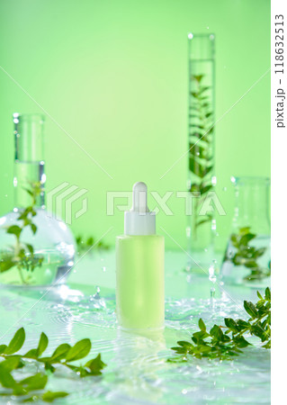 A minimalist advertisement for skincare products features a fresh green background on a wavering water surface, an unlabeled serum bottle, and glass laboratory equipment containing fresh branches. A minimalist advertisement for skincare products features a fresh green background on a wavering water surface, an unlabeled serum bottle, and glass laboratory equipment containing fresh branches. 118632513