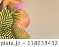 Pregnant woman in pink bikini with belly exposed, tropical leaves in foreground. Pregnancy concept. 118633432